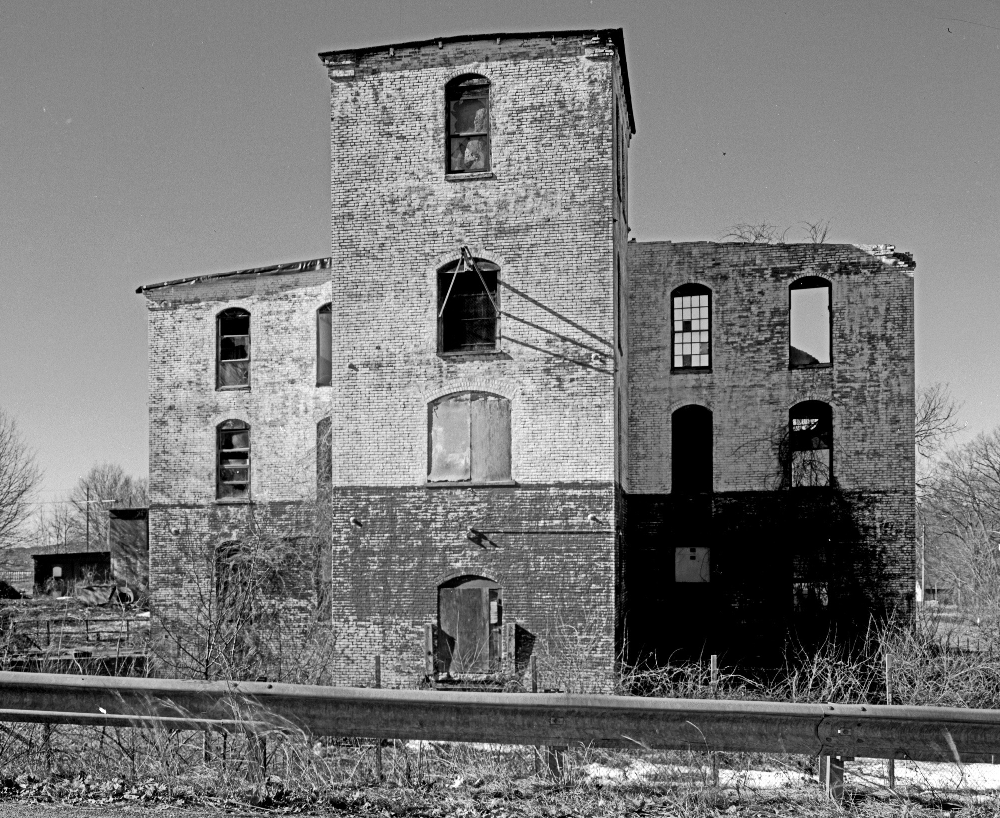 A brick mill building with broken windows and a partially collapsed roof.