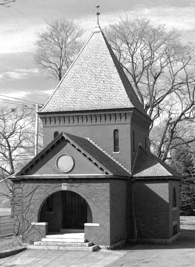 Andrew Barr's documentation photograph of a brick chapel with a steep pyramidal roof and arched entrance, in black and white.
