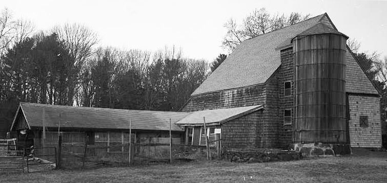 A weathered wood-shingled barn and silo with a sagging attached shed.